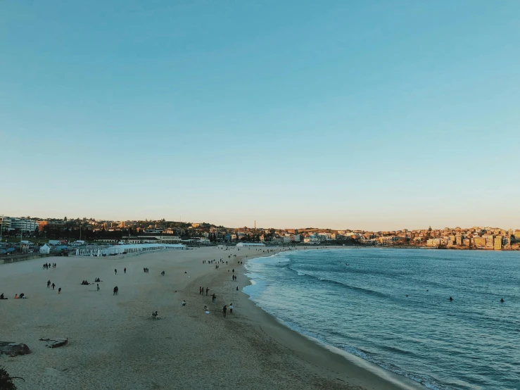 a beach filled with lots of people next to the ocean, by Niko Henrichon, pexels contest winner, bondi beach in the background, evening sunlight, light blue clear sky, trending on vsco