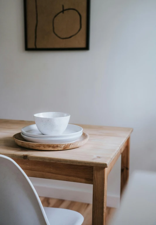 a white plate sitting on top of a wooden table, trending on unsplash, minimalism, table in front with a cup, painting of an undercover cup, bowl, set photo