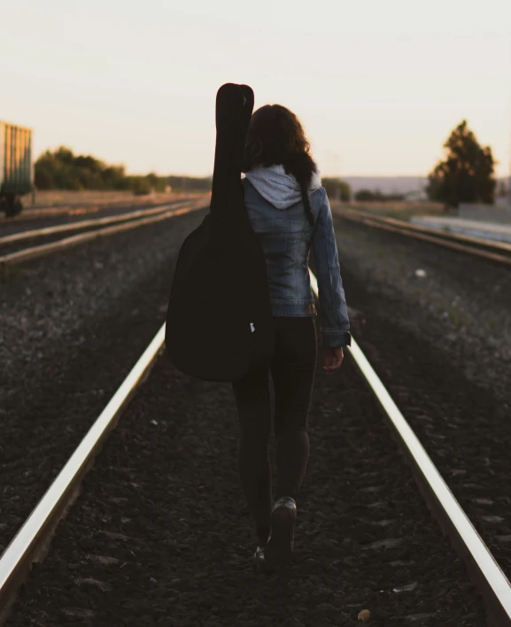 a woman walking down a train track carrying a guitar case, pexels contest winner, happening, non-binary, profile picture, broken down, photo of young woman