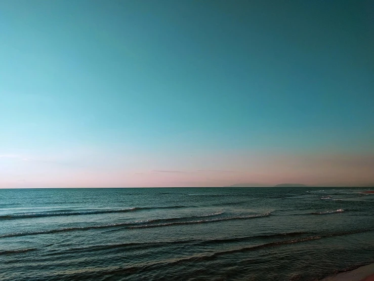 a large body of water next to a beach, inspired by Elsa Bleda, pexels contest winner, minimalism, pink and blue gradients, cloudless sky, late evening, blue - green tones
