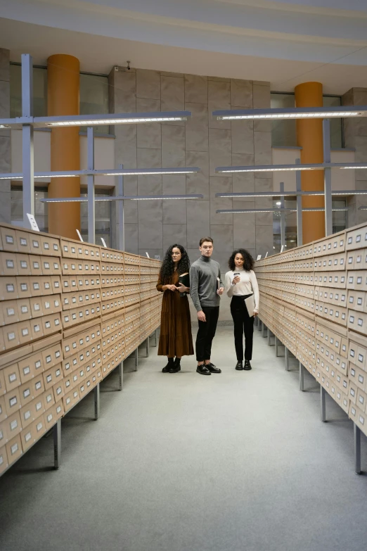 a group of people standing next to each other in a room, an album cover, by Jakob Häne, conceptual art, infinite library, museum lighting, brown, student