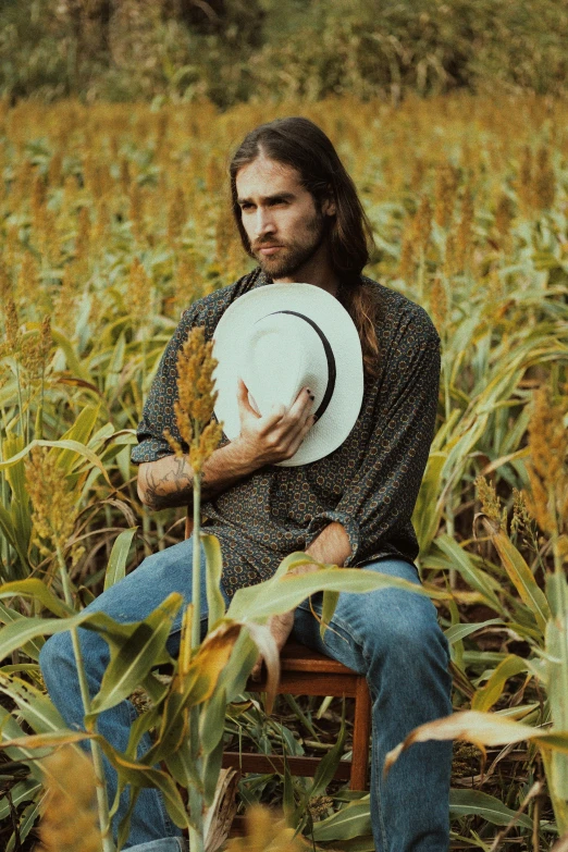 a man sitting in a field with a hat, an album cover, by Jessie Alexandra Dick, pexels contest winner, shoulder long hair, corn, raphael hopper, sitting in a rocking chair