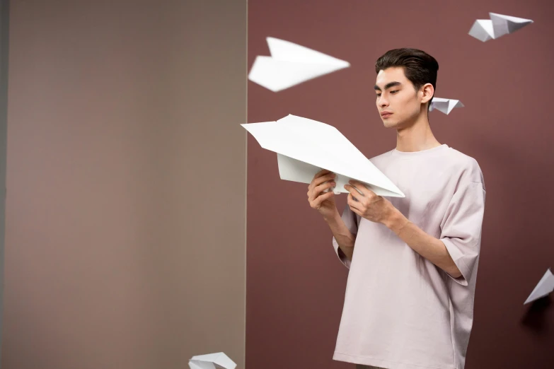 a man standing in front of a wall holding a paper airplane, inspired by Fei Danxu, pexels contest winner, conceptual art, in pastel shades, origami studio 3 design, wearing a light shirt, a handsome