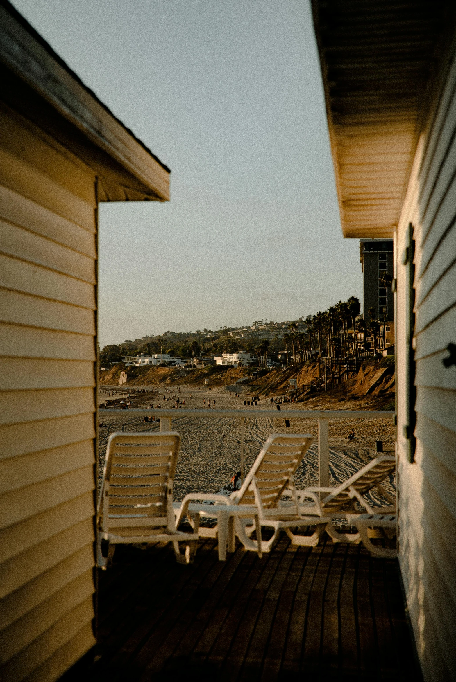 a couple of lawn chairs sitting on top of a wooden deck, by Carey Morris, unsplash, sand - colored walls, several cottages, oceanside, late afternoon