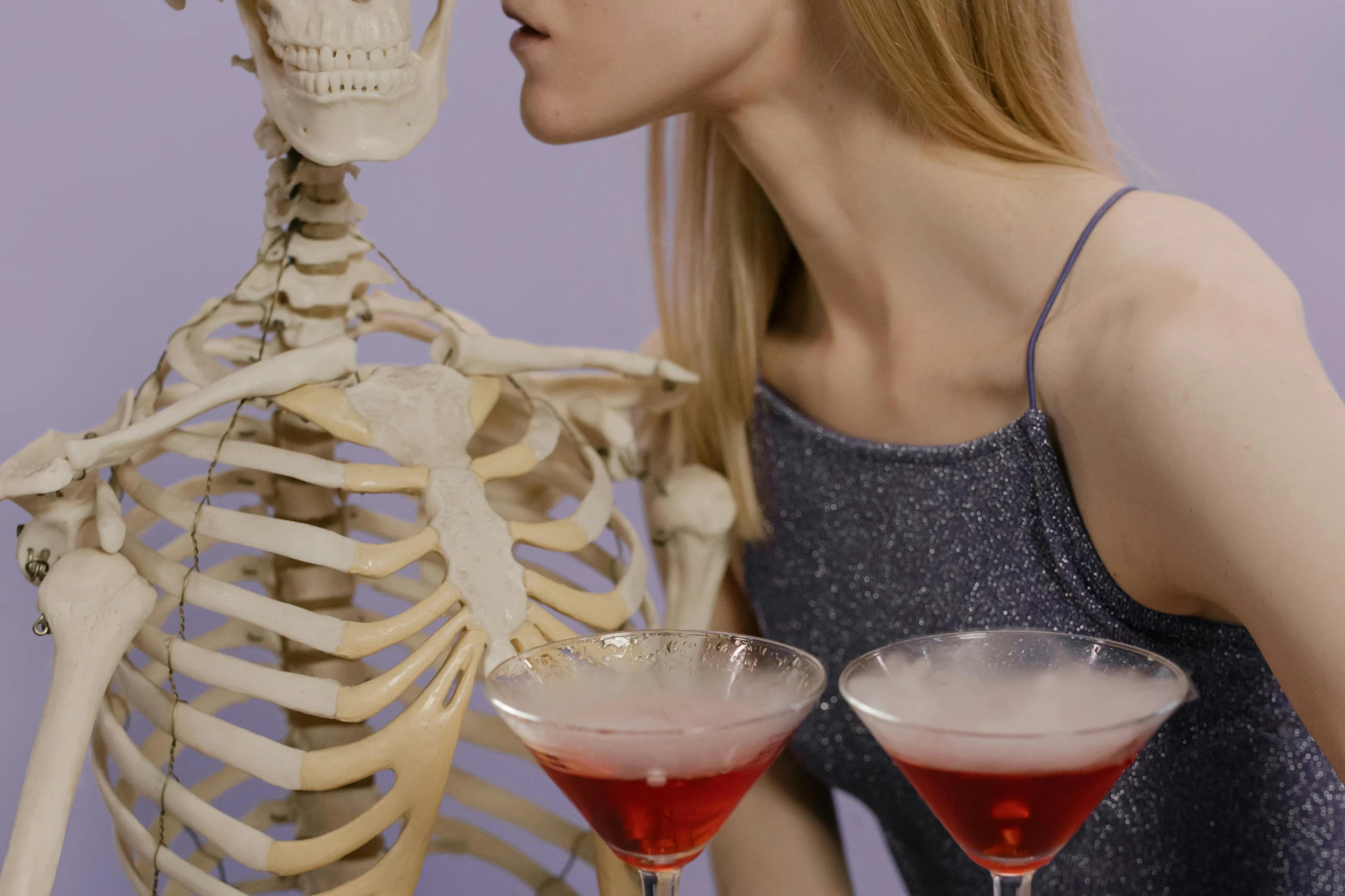 a woman drinking a drink in front of a skeleton, trending on pexels, kinetic art, wearing a cocktail dress, vocal tract model, candy treatments, crimson themed