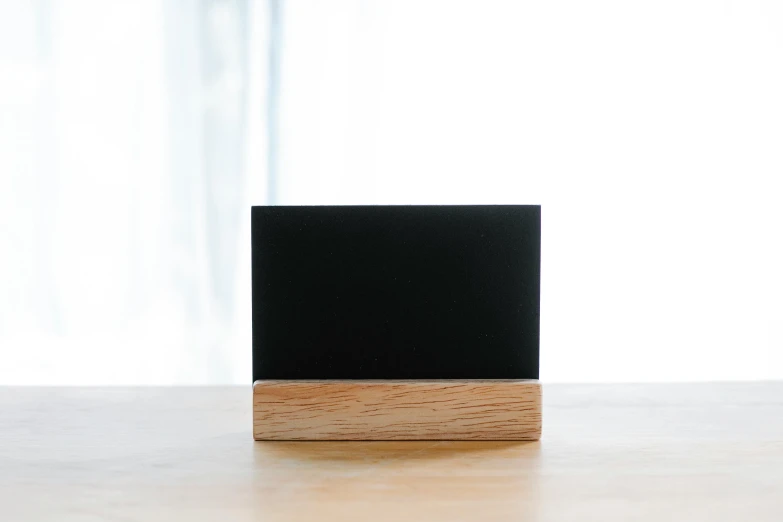 a black square sitting on top of a wooden table, an abstract sculpture, unsplash, blackboard, front left speaker, oak, back facing