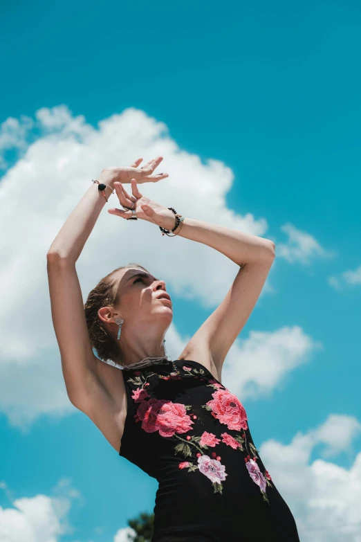 a woman in a black dress reaching up to catch a frisbee, unsplash, arabesque, blue sky above, photo of a hand jewellery model, ballet style pose, looking off into the distance