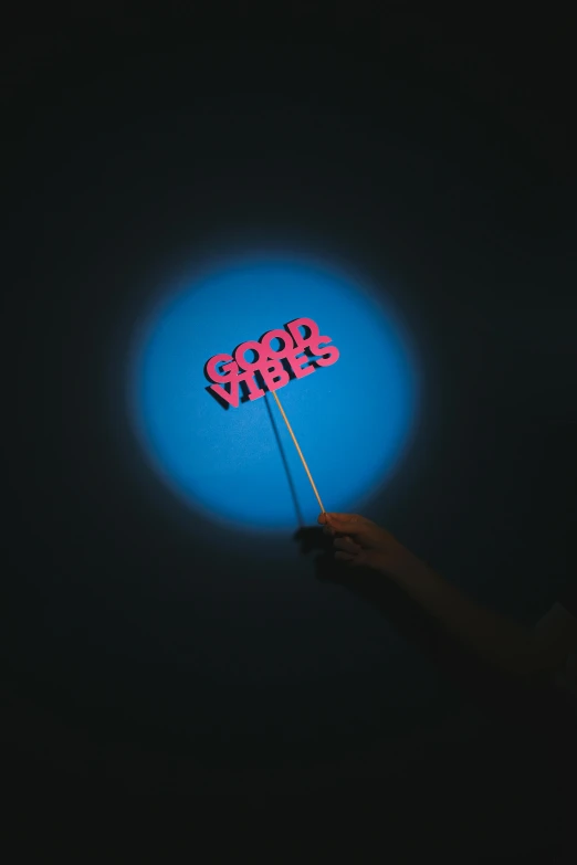 a person holding up a neon sign in the dark, an album cover, by Jacob Toorenvliet, unsplash, holding the moon upon a stick, good vibes, light red and deep blue mood, lollipops