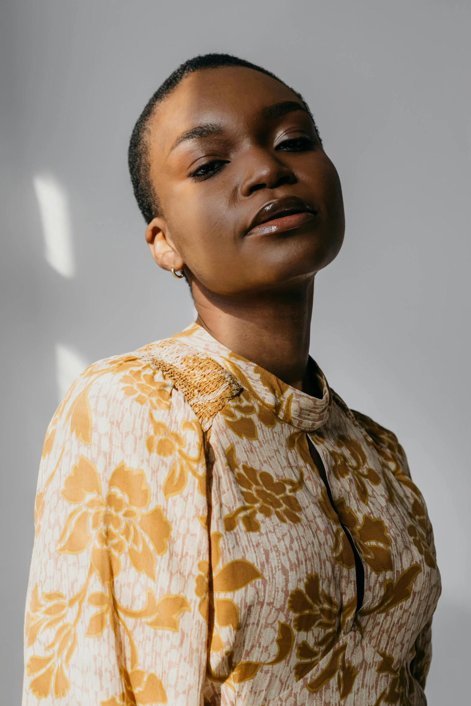 a woman standing in front of a white wall, trending on pexels, renaissance, wearing yellow floral blouse, dark skin tone, refined editorial photograph, robe. perfect face