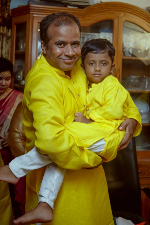 a man holding a child in his arms, an album cover, inspired by Odhise Paskali, yellow robes, unedited, at home, in 2 0 1 5