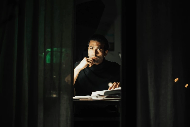 a man sitting at a table reading a book, a portrait, pexels contest winner, green light coming from window, joe taslim, pitch black room, raphael lecoste