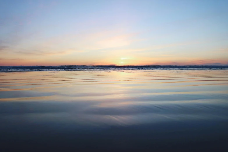 a man riding a surfboard on top of a sandy beach, by Jessie Algie, unsplash contest winner, minimalism, sunset panorama, blue reflections, ripples, photo of the middle of the ocean