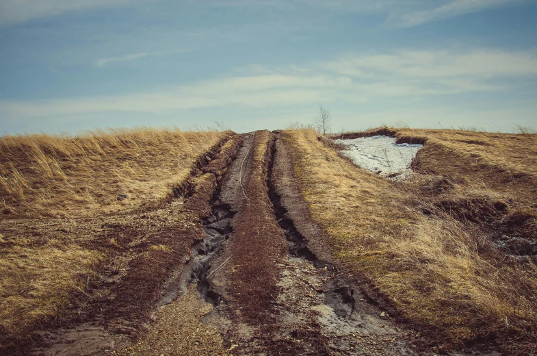 a dirt road in the middle of a field, an album cover, unsplash, land art, spring winter nature melted snow, landslides, stålenhag, historical photo