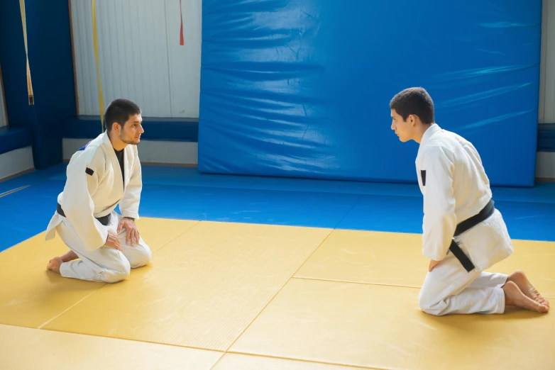 a couple of men sitting on top of a yellow floor, martial arts, square, private school, featured