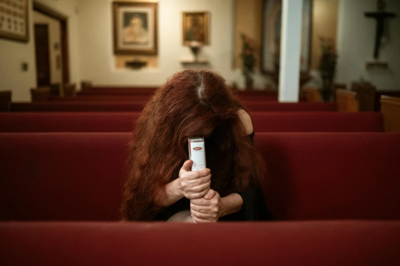 a woman sitting in a church holding a cell phone, inspired by Nan Goldin, long red hair, ap news, funeral, photo illustration