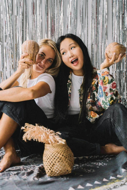 a couple of women sitting next to each other, a portrait, inspired by Wang Duo, trending on unsplash, kitsch movement, sitting on the floor, polinesian style, wearing seashell attire, one blonde and one brunette