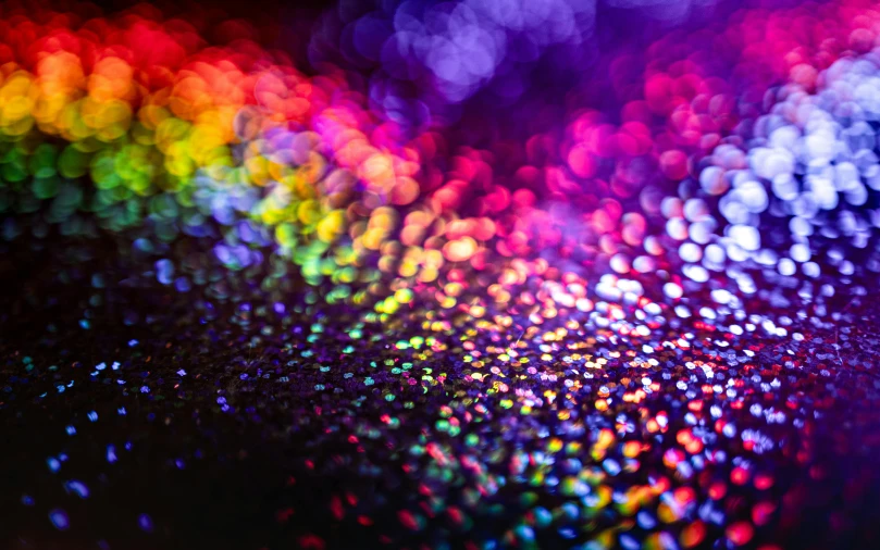 a rainbow colored light shines brightly on a black surface, a microscopic photo, by Julia Pishtar, unsplash, sequins, purple sparkles, rainbow road, glistening skin