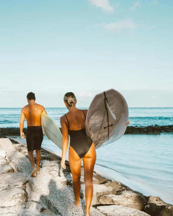 a couple of people walking on a beach with surfboards, back facing the camera, tanned skin, reefs, karolina cummings