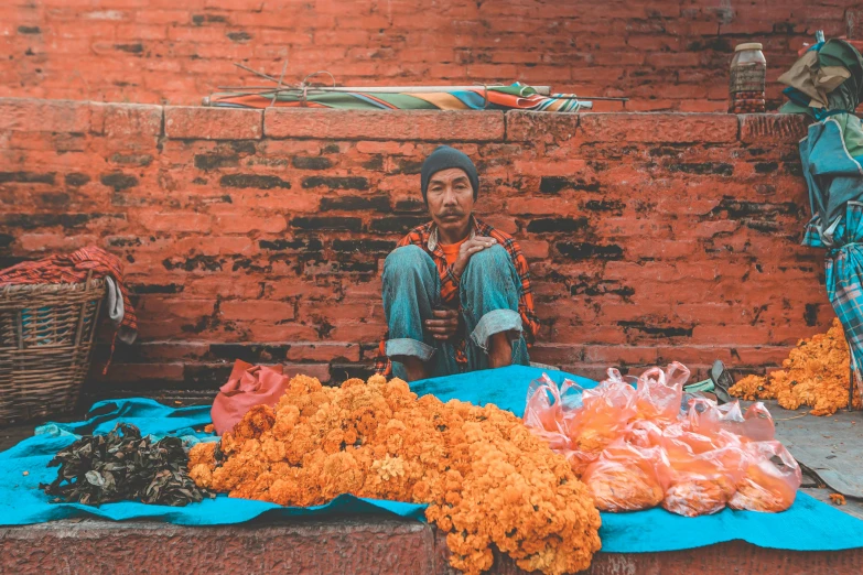 a man sitting in front of a pile of flowers, inspired by Steve McCurry, pexels contest winner, hurufiyya, street vendors, teal and orange, nepal, 🦩🪐🐞👩🏻🦳