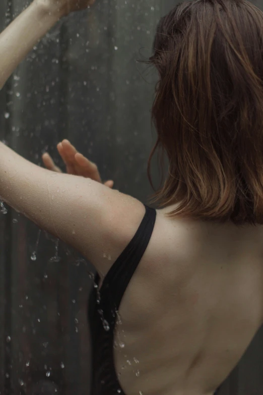 a woman in a bathing suit standing in front of a shower, trending on unsplash, renaissance, rainy outside, showing her shoulder from back, she is wearing a black tank top, ignant