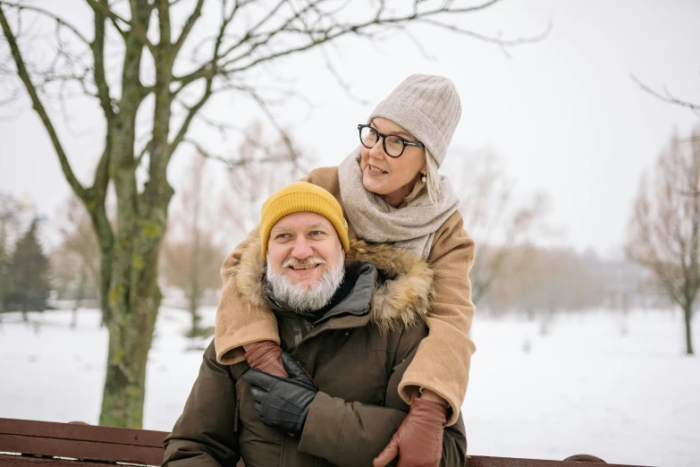 a man and woman sitting on a bench in the snow, bald head and white beard, looking happy, avatar image, winter photograph