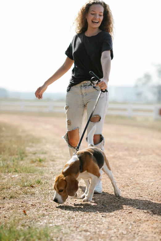 a woman walking a dog on a leash, trending on pexels, jeans and t shirt, on a farm, australian, cute beagle