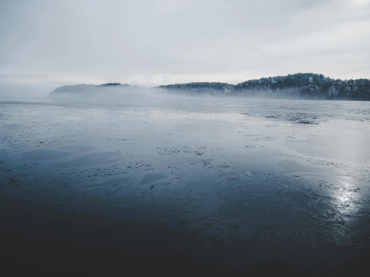 a large body of water sitting on top of a sandy beach, pexels contest winner, romanticism, in an icy river, black fog, espoo, blue and gray colors