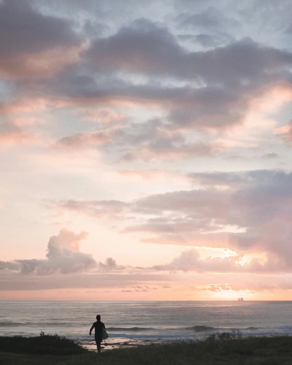 a man riding a surfboard on top of a sandy beach, by Maggie Hamilton, unsplash contest winner, minimalism, sunset panorama, pink and grey clouds, waikiki beach, man sitting facing away