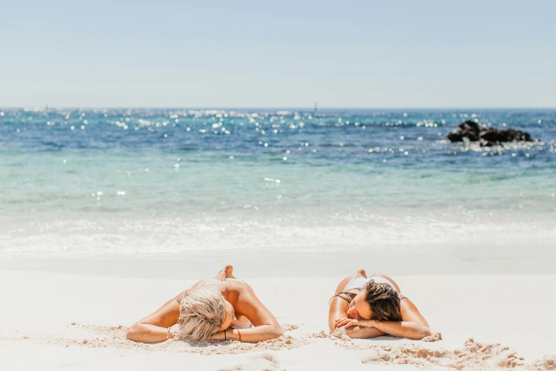 a couple of women laying on top of a sandy beach, pexels contest winner, minimalism, skincare, sparkling in the sunlight, australian beach, 💋 💄 👠 👗