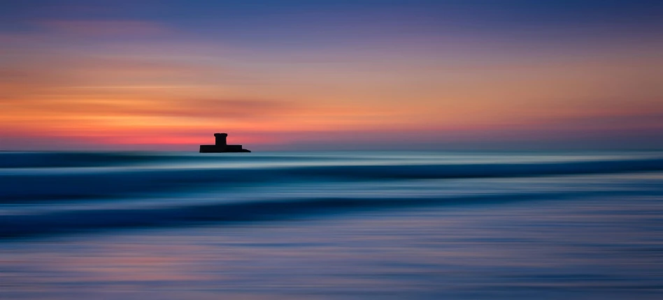 a lighthouse in the middle of the ocean at sunset, by Andrew Bell, minimalism, multi - coloured, surf photography, watch tower, orton effect