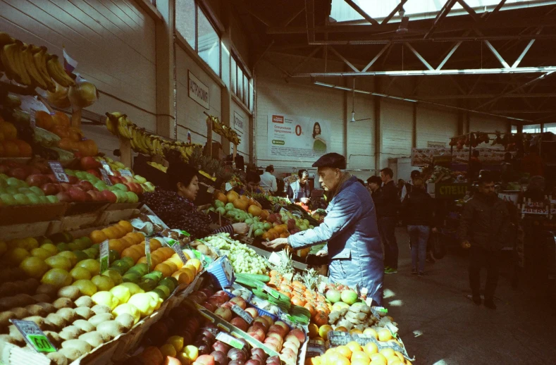 a man standing in front of a display of fruits and vegetables, a photo, by Nathalie Rattner, unsplash, some stalls, overexposed sunlight, chilean, inside the building
