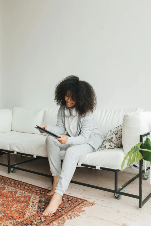 a woman sitting on a couch reading a book, by Matija Jama, wearing a track suit, long afro hair, tech robes, white grey color palette