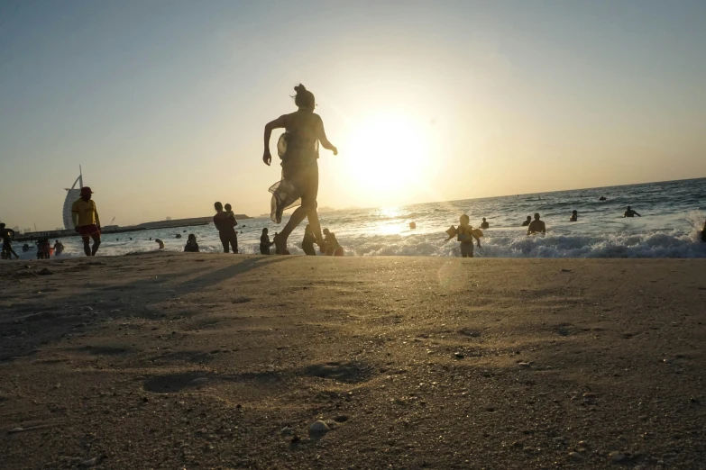 a group of people standing on top of a sandy beach, during a sunset, people running, jamel shabbaz, in the sea