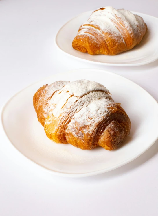 two croissants on white plates on a table, by Carlo Martini, 3 - piece, frosted, various sizes, 2. 5 - dimensional