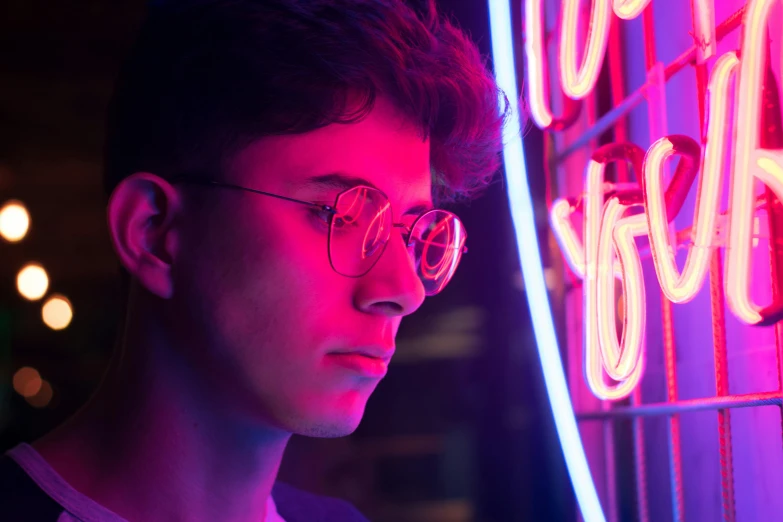 a man standing in front of a neon sign, pexels contest winner, jewish young man with glasses, declan mckenna, pensive, 80s outrun