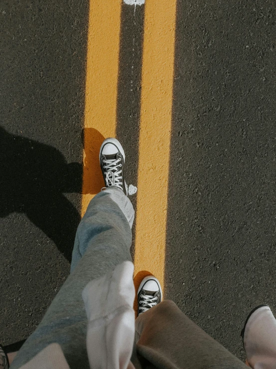 a person standing on a street with their feet on a skateboard, trending on pexels, realism, black and yellow, shot from 5 0 feet distance, wearing white sneakers, on a road