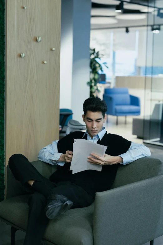 a man sitting in a chair reading a piece of paper, gen z, office clothes, male teenager, ignant