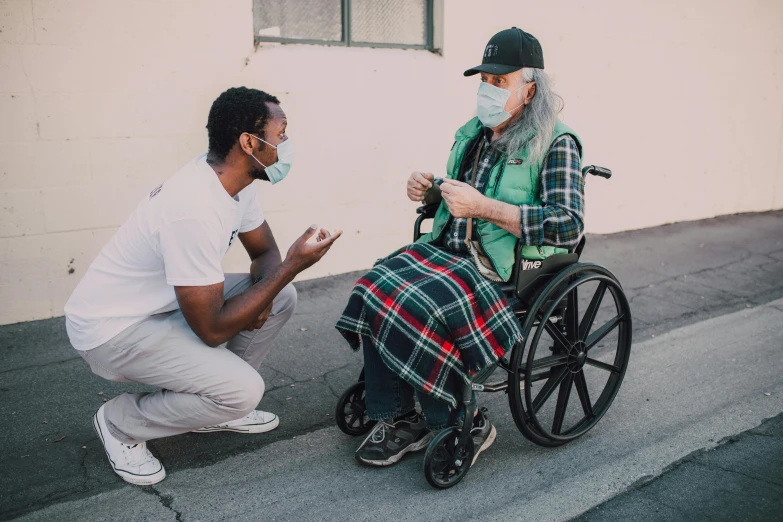 a man in a wheelchair talking to a man in a face mask, a photo, by Dan Frazier, pexels contest winner, tyler the creator, two frail, medium long shot, jovana rikalo