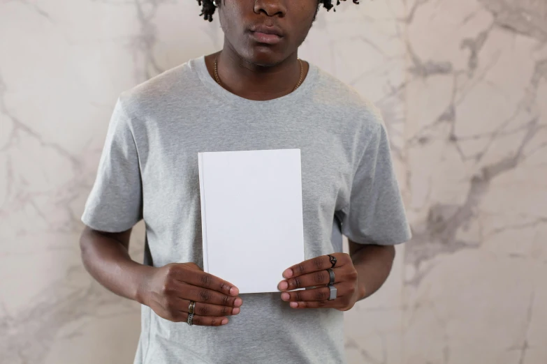 a man holding a piece of paper in his hands, an album cover, by Joseph Severn, pexels contest winner, private press, plain white tshirt, dark-skinned, pale grey skin, holding notebook
