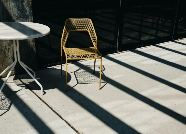 a yellow chair sitting next to a white table, inspired by William Berra, unsplash contest winner, dappled afternoon sunlight, perforated metal, hexagonal shaped, eating outside