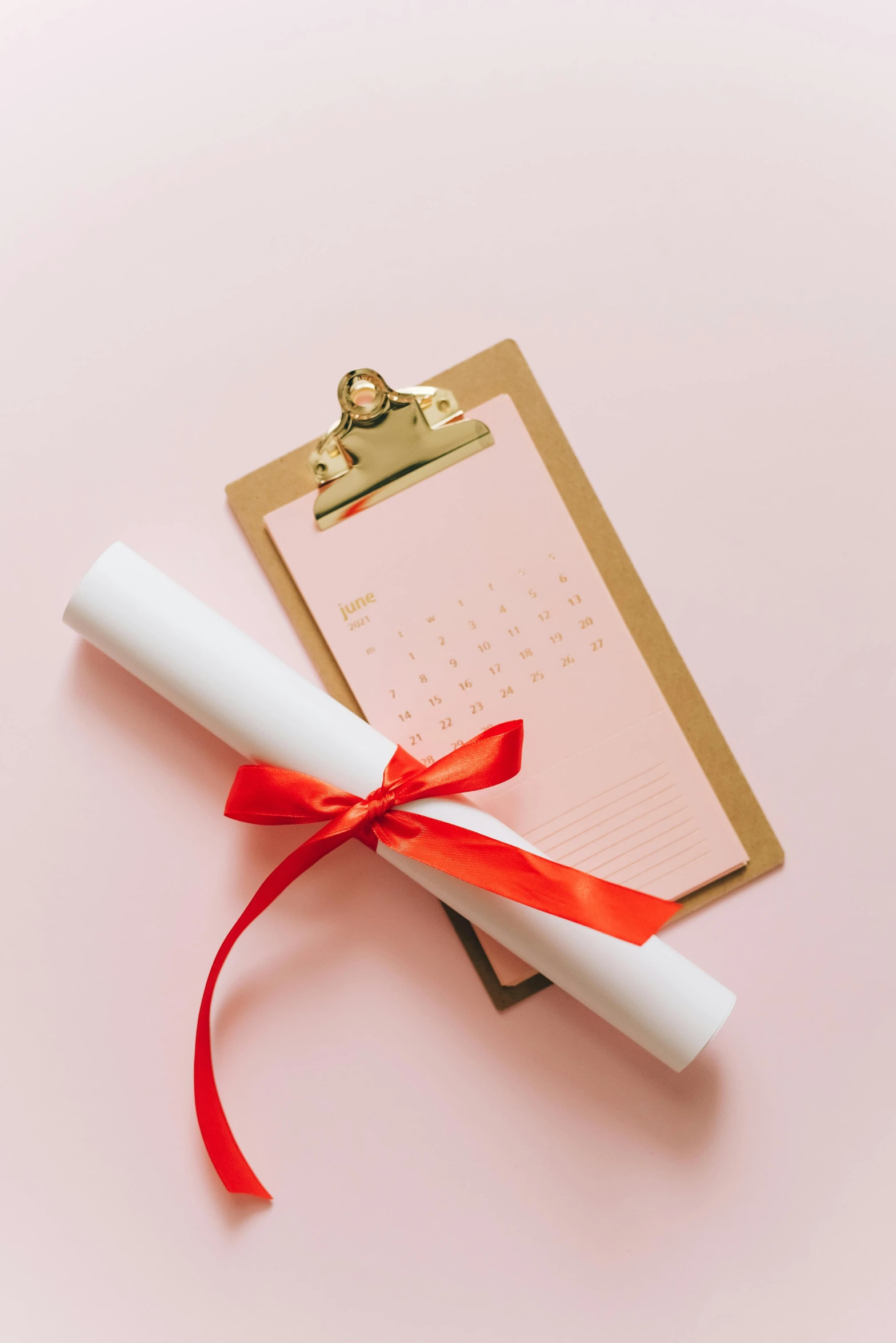 a graduation diploma laying on top of a clipboard, by Julia Pishtar, pexels contest winner, pink and red color scheme, female calendar, golden ribbon, thumbnail