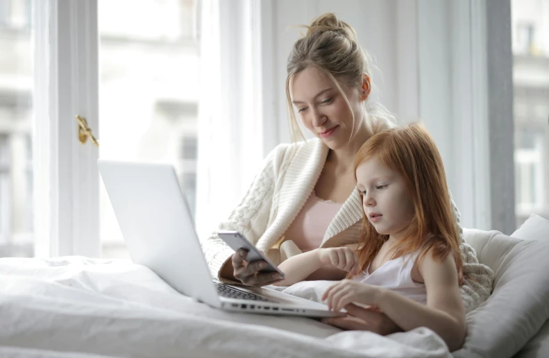 a woman and a little girl sitting on a bed with a laptop, pexels, avatar image, 1 5 0 4, white, checking her phone