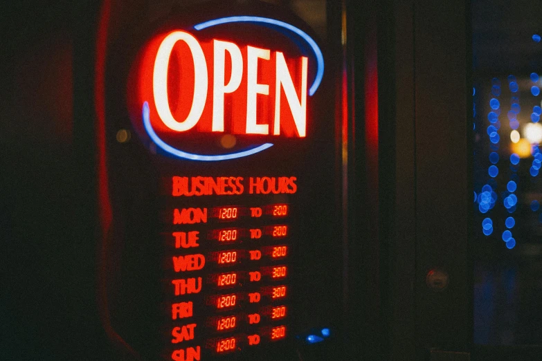 a red and blue open sign sitting on the side of a building, a photo, pexels, midnight hour, shop front, open bank vault, busy night