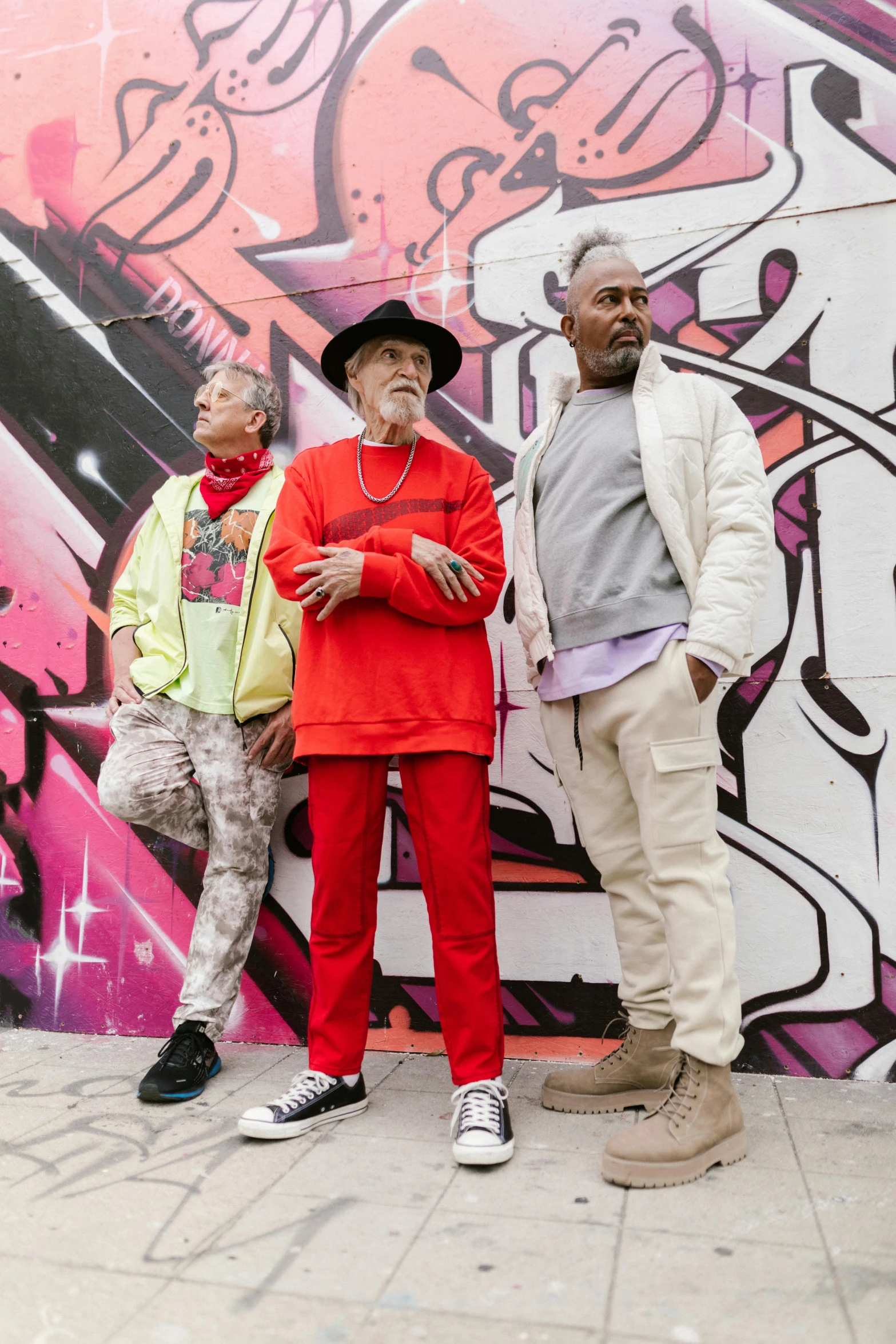 three men standing in front of a graffiti covered wall, inspired by Edwin Georgi, graffiti, red clothes, two old people, wearing off - white style, multicoloured