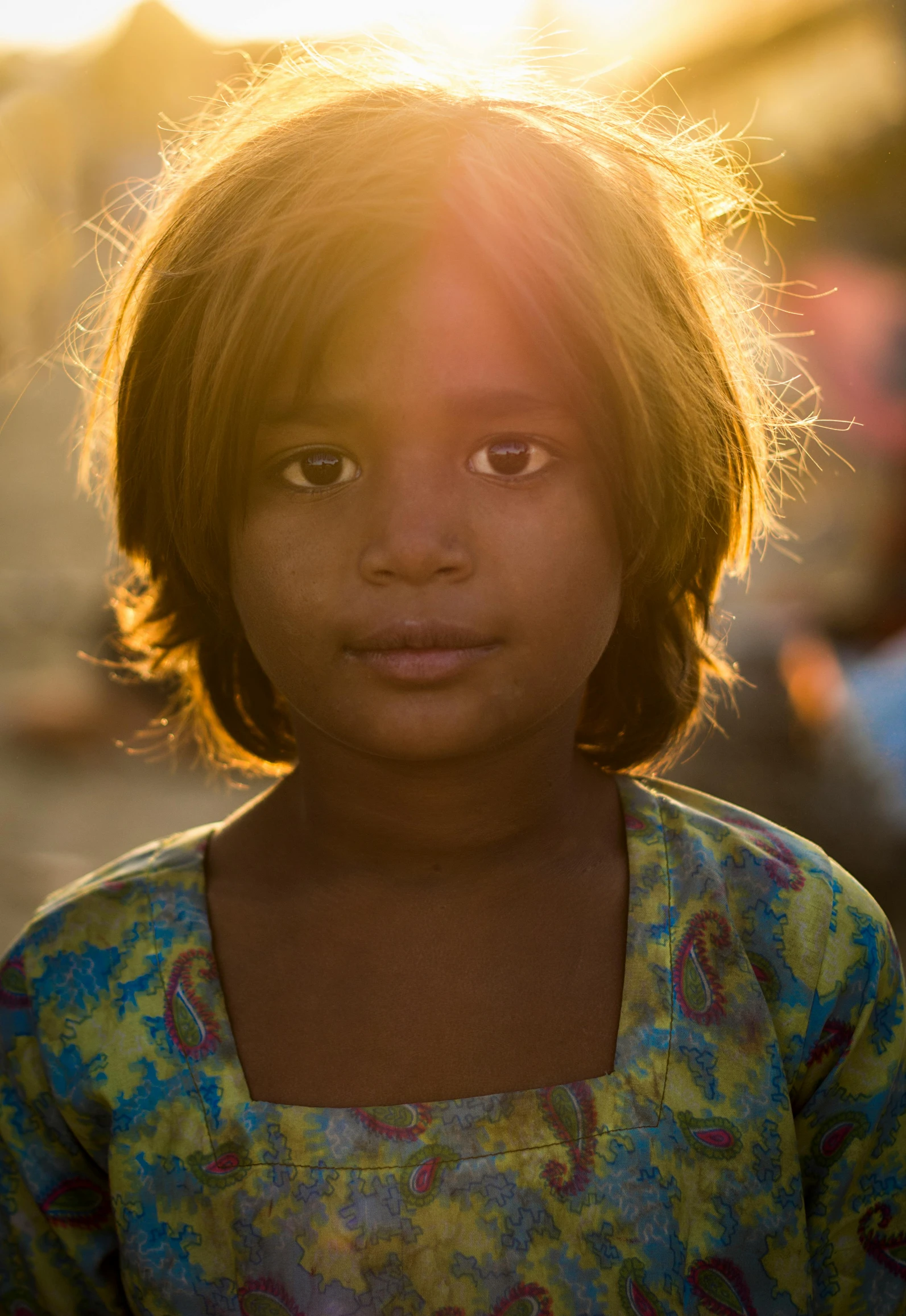 a little girl that is looking at the camera, by Rajesh Soni, late afternoon sun, multicoloured, afar, face illuminated