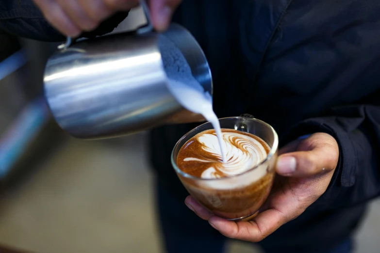 a person pouring milk into a cup of coffee, by Lee Loughridge, unsplash, 9 9 designs, aussie baristas, “ iron bark, from the elbow