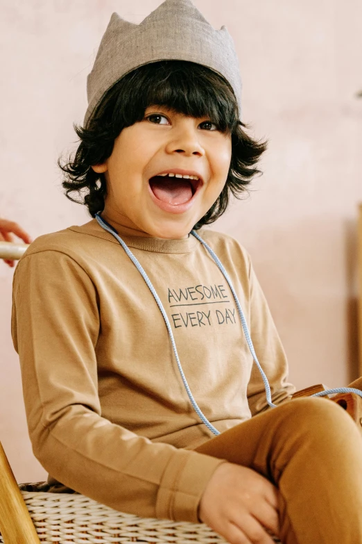 a little boy sitting on top of a wooden chair, trending on pexels, earing a shirt laughing, beige hoodie, thumbnail, chocolate