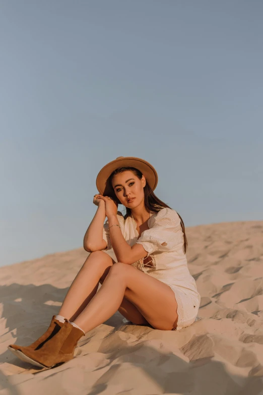 a woman sitting on top of a sandy beach, a portrait, by Julia Pishtar, trending on pexels, charli xcx, beige fedora, doing a hot majestic pose, sittin