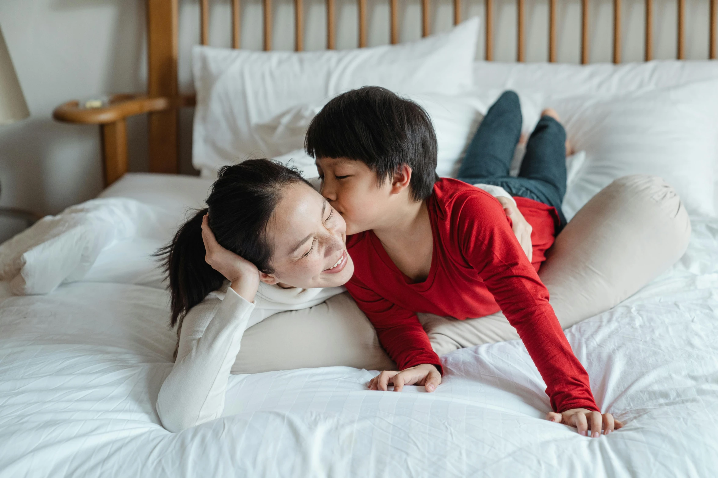 a woman laying on top of a bed next to a boy, pexels contest winner, kissing together cutely, asian, mom, ad image