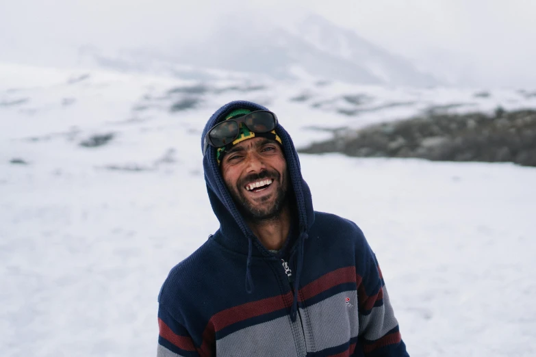a man standing on top of a snow covered slope, pexels contest winner, hurufiyya, brown skin man with a giant grin, a portrait of rahul kohli, wearing sunglasses and a cap, norwegian man